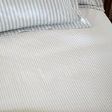 Hebden Striped Cotton Fitted Sheet in Mineral Blue, fitted over a mattress with matching pillowcase, showing a narrow blue and white stripe on cotton fabric.