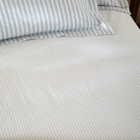Hebden Striped Cotton Fitted Sheet in Mineral Blue, fitted over a mattress with matching pillowcase, showing a narrow blue and white stripe on cotton fabric.