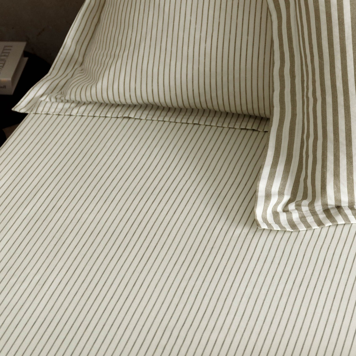 Hebden Striped Cotton Fitted Sheet in mole, made up on a bed with matching pillowcase, showing fine taupe-grey pinstripes on a cream cotton ground.