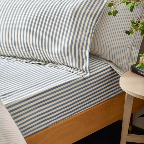Hebden Reversible Cotton Fitted Sheet on a wooden bed frame, showing a navy and cream striped pattern with matching pillowcases in a bedroom setting.