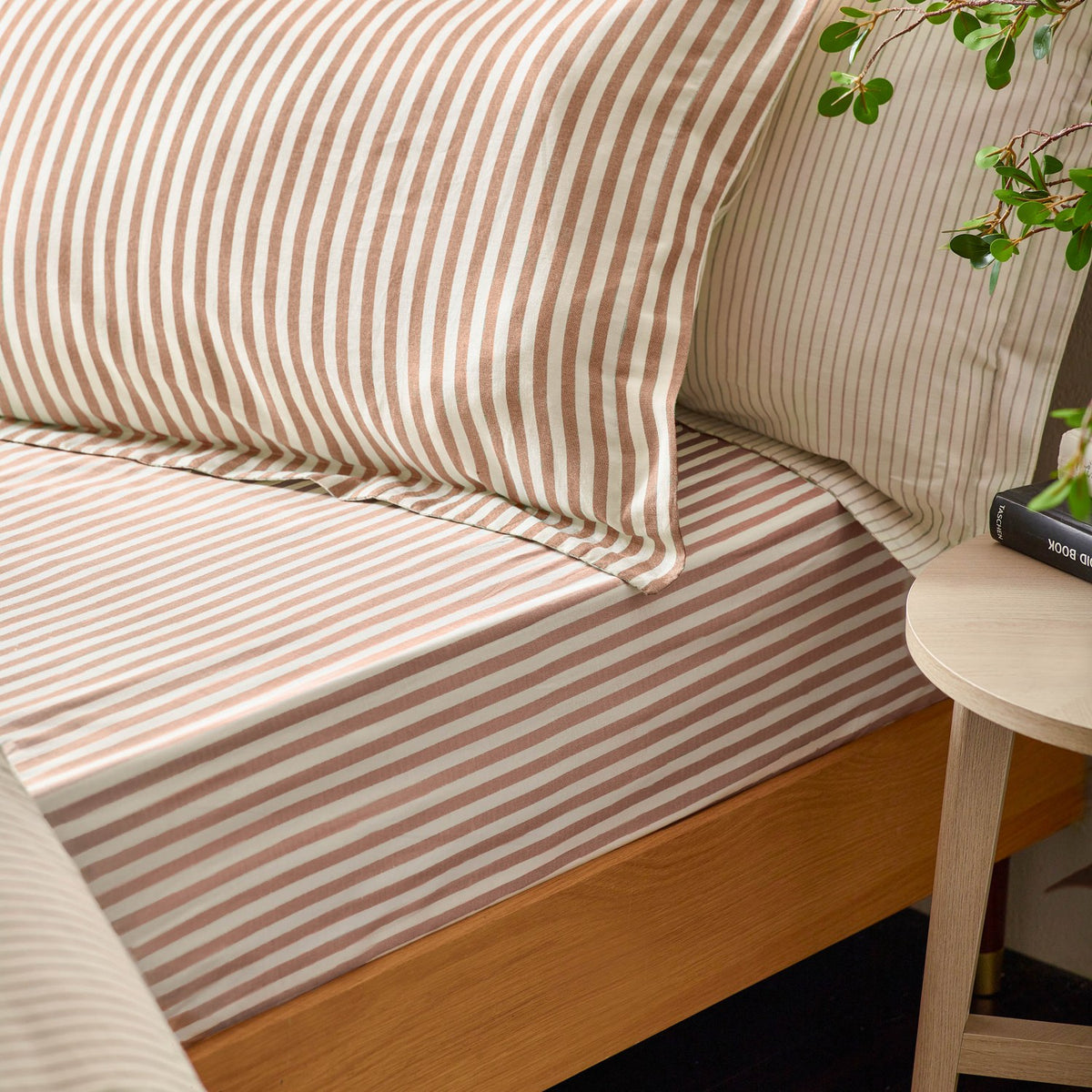Hebden Cotton Fitted Sheet in cream with pecan and terracotta stripes, shown fitted on a wooden bed frame with matching striped pillowcases in a bedroom setting.