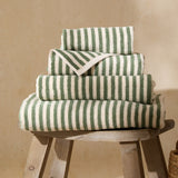 Hebden Striped Cotton Towels in Forest, four folded green and cream striped cotton towels stacked in varying sizes on a wooden stool.