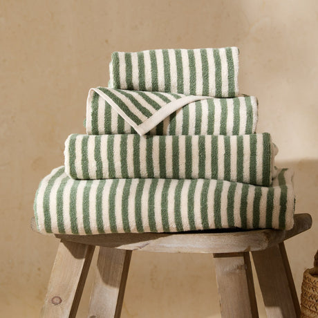 Hebden Striped Cotton Towels in Forest, four folded green and cream striped cotton towels stacked in varying sizes on a wooden stool.
