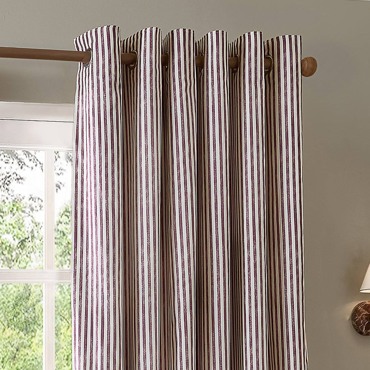 Hebden Cotton Printed Eyelet Curtains in Beetroot, showing cream fabric with fine vertical red stripes, hung on a wooden pole with metal eyelets in a room setting.