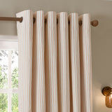 Hebden Cotton Printed Eyelet Curtains in Blush, striped cotton panels with brass eyelets hung on a wooden pole beside a window in a bedroom setting.