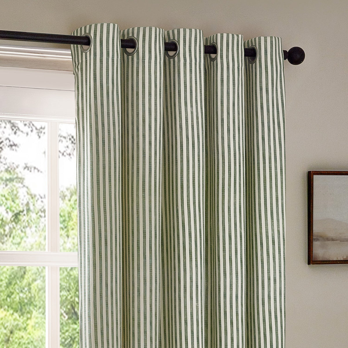 Hebden Cotton Printed Eyelet Curtains in Forest, showing a metal eyelet header on a black pole, in forest green and off-white striped cotton fabric, hung beside a window.