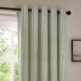 Hebden Cotton Printed Eyelet Curtains in Forest, showing a metal eyelet header on a black pole, in forest green and off-white striped cotton fabric, hung beside a window.