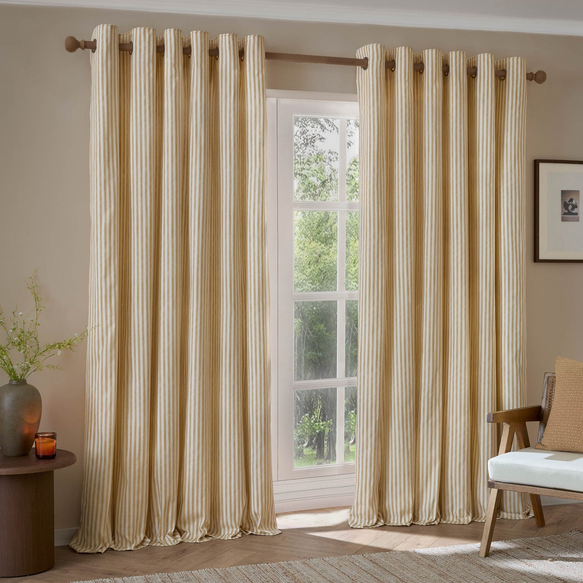 Hebden Cotton Printed Eyelet Curtains in honey yellow and off-white vertical stripe, hung on a wooden pole beside a window in a living room setting.