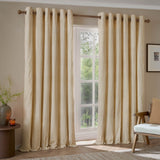 Hebden Cotton Printed Eyelet Curtains in honey yellow and off-white vertical stripe, hung on a wooden pole beside a window in a living room setting.