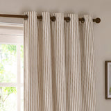 Hebden Cotton Printed Eyelet Curtains in natural stripe, hung on a bronze pole with round metal eyelets, shown against a window in a living room setting.
