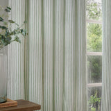 Hebden Striped Cotton Pencil Pleat Curtains in eucalyptus green on pale ground, shown hanging at a window beside a wooden table and potted greenery.