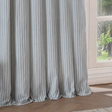 Hebden Striped Cotton Pencil Pleat Curtains in Mineral Blue, showing pale blue and white vertical stripes with a gathered header, styled beside a window in a living room.