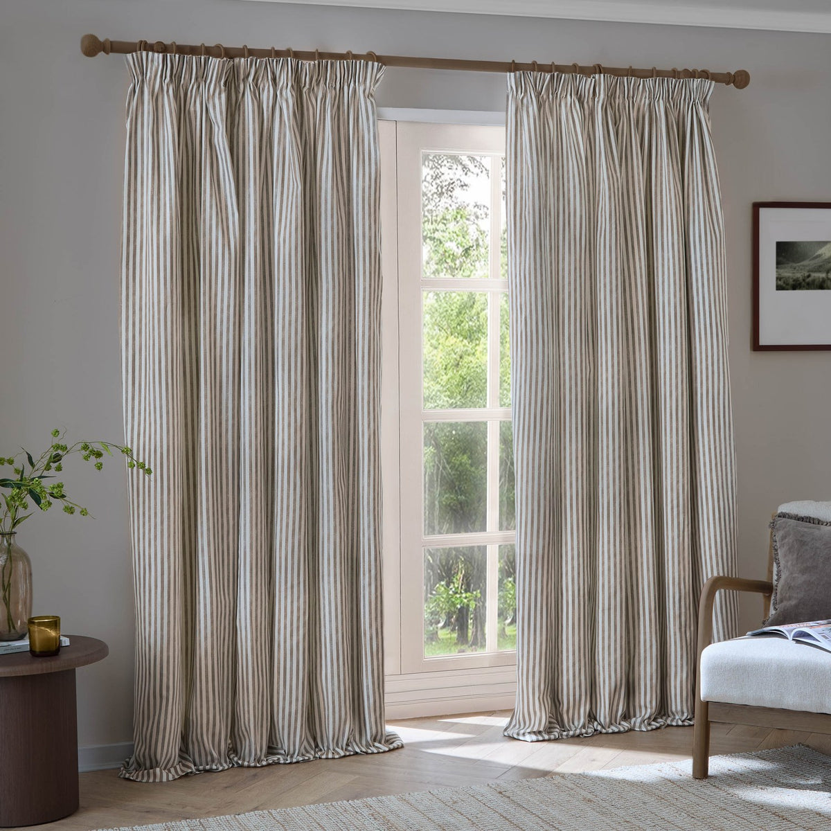 Hebden Striped Cotton Pencil Pleat Curtains in Mole hang from a wooden pole, showing fine mole-brown ticking stripes on pale cotton with a pencil pleat header.
