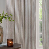 Hebden Striped Cotton Pencil Pleat Curtains in mole-brown stripe on cream, hung floor-length beside a window, styled with a glass vase and candle on a side table.