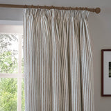 Hebden Striped Cotton Pencil Pleat Curtains in mole-brown and cream ticking stripe, hung on a wooden pole with pleated header, shown beside a window in a living room.