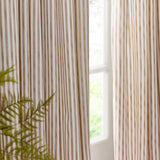 Hebden pencil pleat curtains in natural cotton stripe, hanging beside a window with soft daylight and a green fern in the foreground.