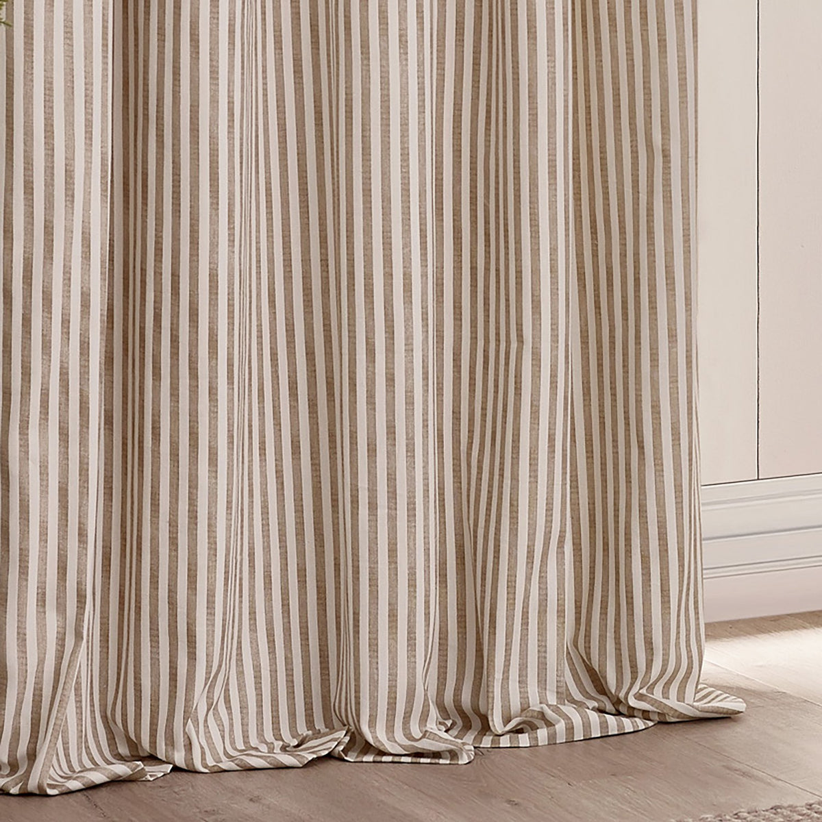 Hebden pencil pleat curtains in natural tan and off-white vertical stripe, 100% cotton fabric falling in gathered folds beside a light wall and wooden floor.