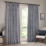 Hebden Striped Cotton Pencil Pleat Curtains in navy and white, hung floor-length beside a window in a living room with an armchair and side table.