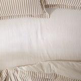 Hebden Striped Cotton Fitted Sheet in Caramel, showing a fine caramel pinstripe on a soft white cotton ground across a fitted sheet and matching pillowcases.