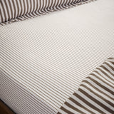 Hebden fitted sheet on a bed, pure cotton with a narrow espresso brown stripe on an off-white ground, elasticated corners fitted over the mattress.