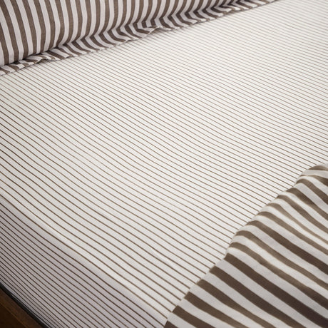 Hebden fitted sheet on a bed, pure cotton with a narrow espresso brown stripe on an off-white ground, elasticated corners fitted over the mattress.
