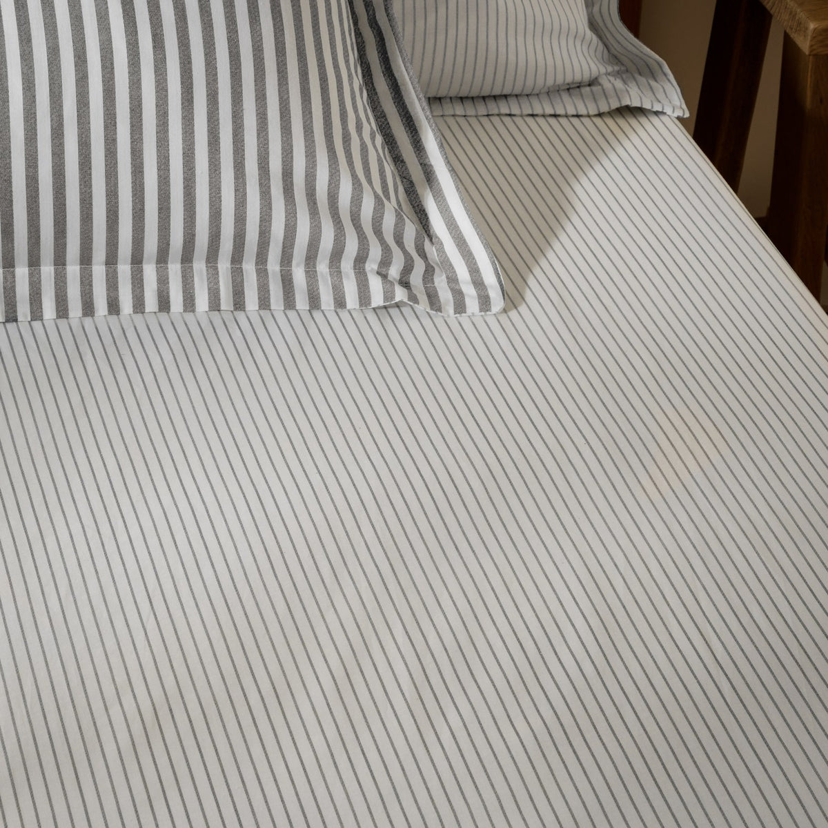 Hebden Striped Cotton Fitted Sheet in grey, shown on a made bed with matching striped pillowcases, pure cotton fabric with a fine woven stripe.