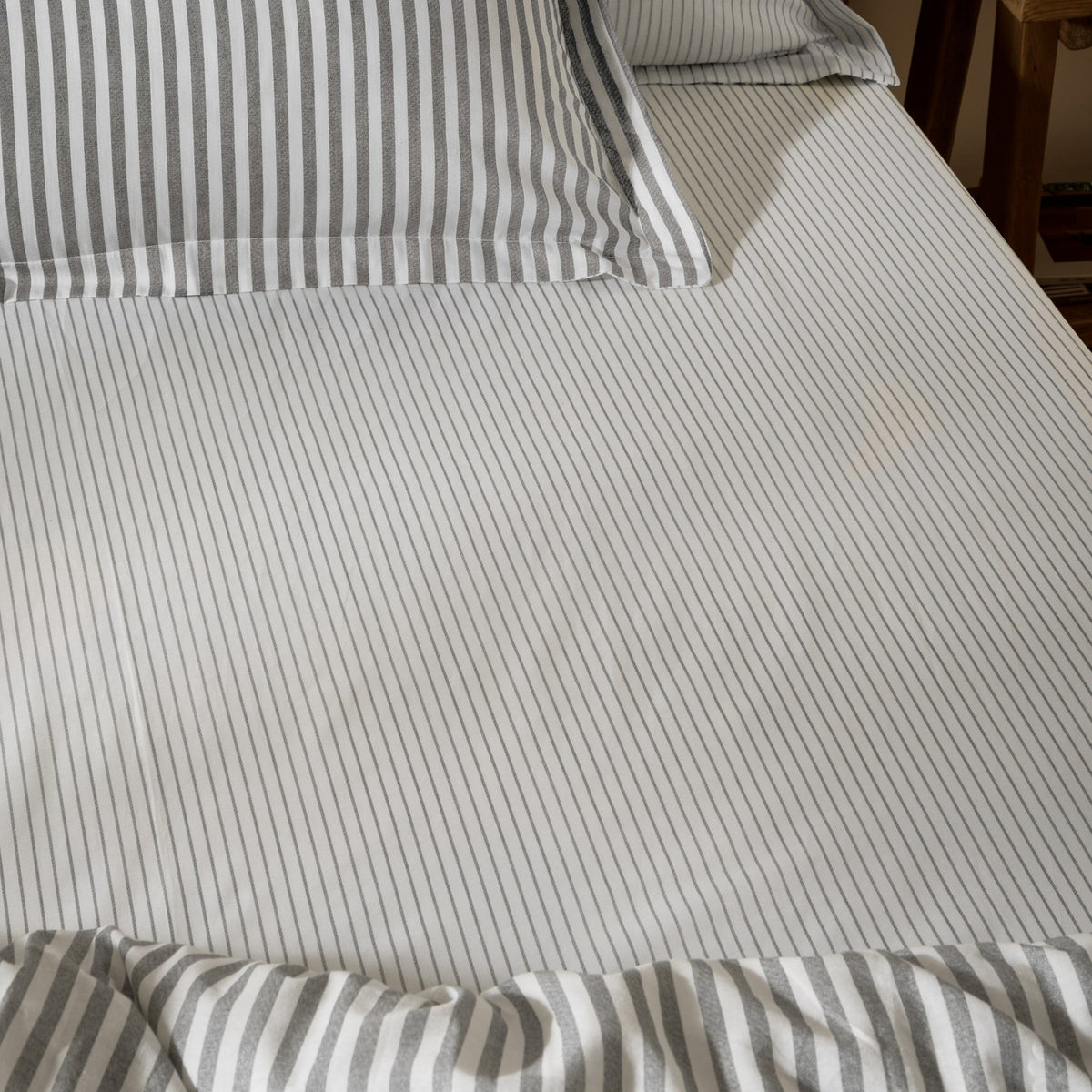 Hebden Striped Cotton Fitted Sheet in grey, shown on a bed with matching striped pillowcases, featuring narrow grey stripes on white cotton fabric.