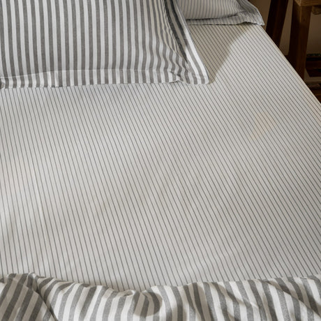 Hebden Striped Cotton Fitted Sheet in grey, shown on a bed with matching striped pillowcases, featuring narrow grey stripes on white cotton fabric.