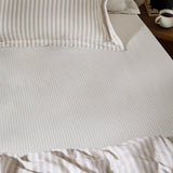 Hebden Striped Cotton Fitted Sheet in natural on a bedroom mattress, showing narrow taupe stripes on cream cotton with matching pillowcase and duvet.