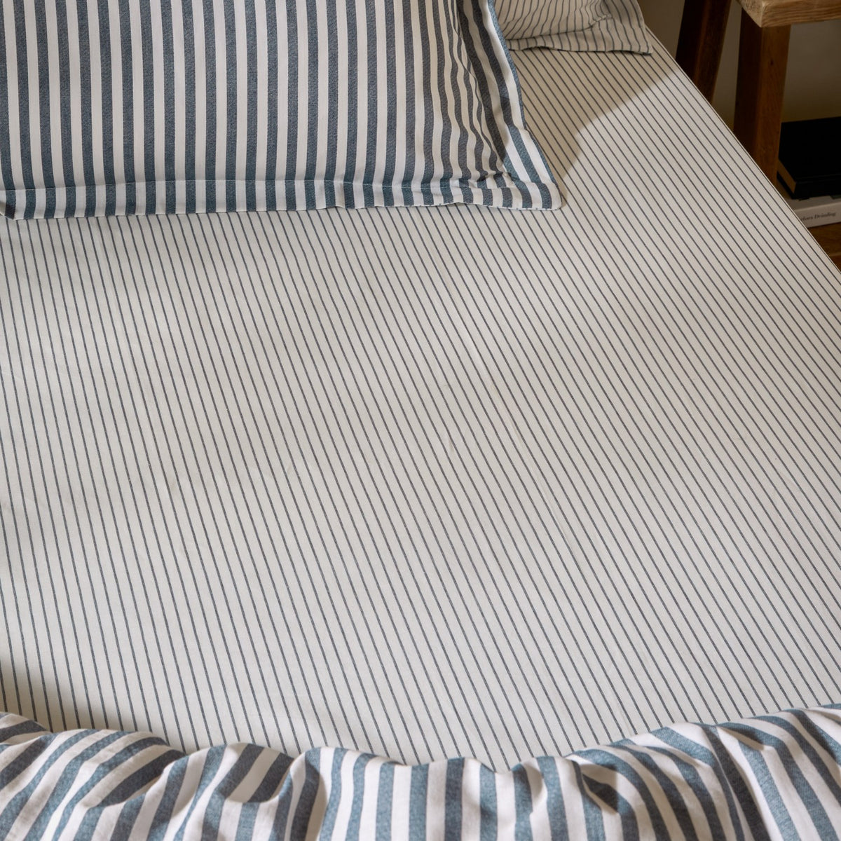 Hebden striped cotton fitted sheet in navy, shown fitted on a bed with matching striped pillowcases and duvet, fine navy stripes on an ivory ground.