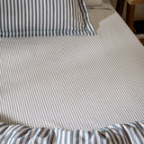 Hebden striped cotton fitted sheet in navy, shown fitted on a bed with matching striped pillowcases and duvet, fine navy stripes on an ivory ground.