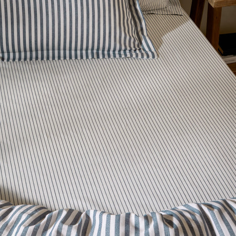 Hebden striped cotton fitted sheet in navy, shown fitted on a bed with matching striped pillowcases and duvet, fine navy stripes on an ivory ground.
