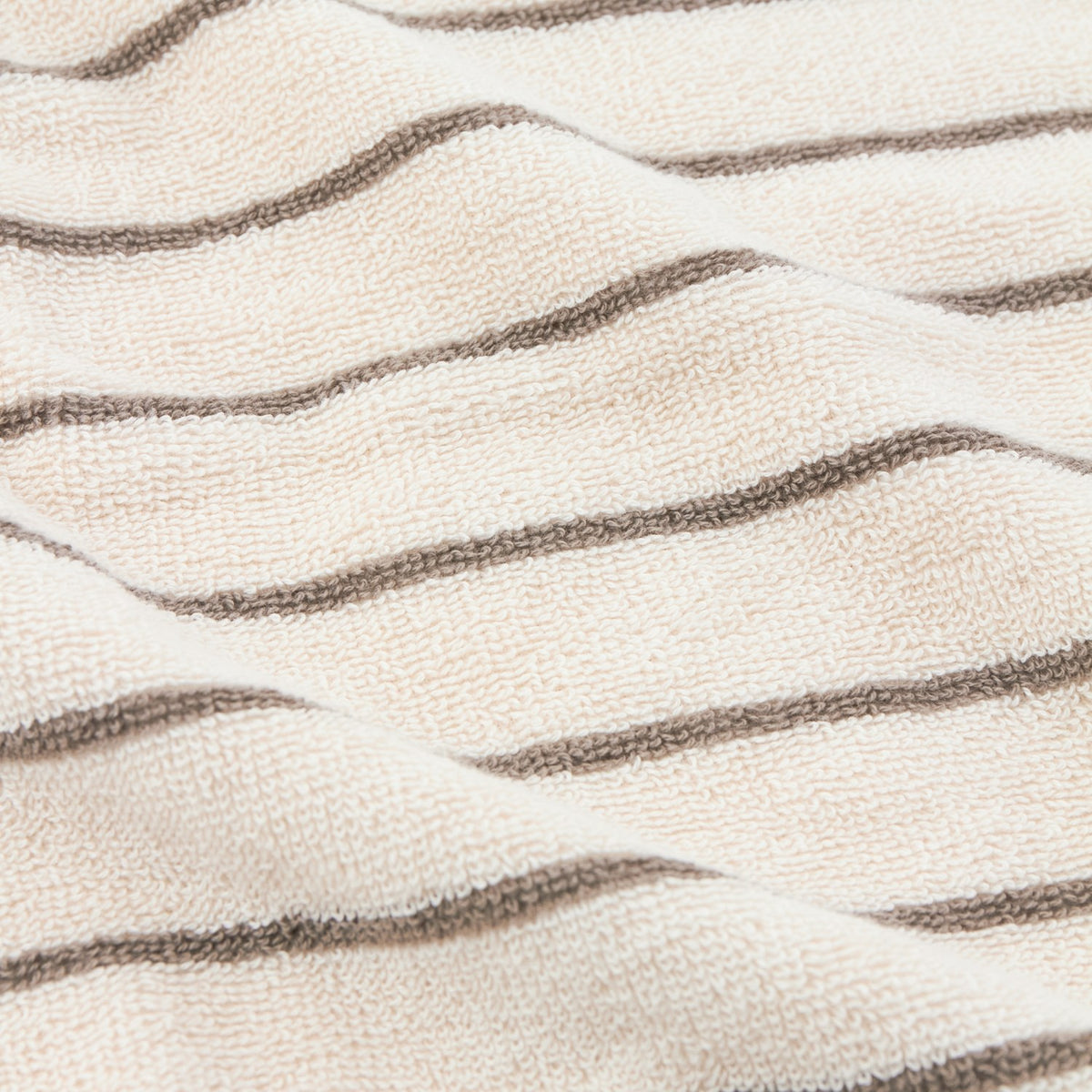 Close-up of the Hebden Striped Cotton Towel in Mole, showing textured cream terry fabric with slim, evenly spaced greyish-brown stripes running lengthwise.