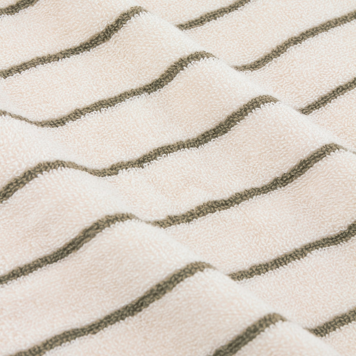 Close-up of the Hebden Striped Cotton Towel in olive, showing narrow green stripes on a cream terry pile fabric folded in soft waves.
