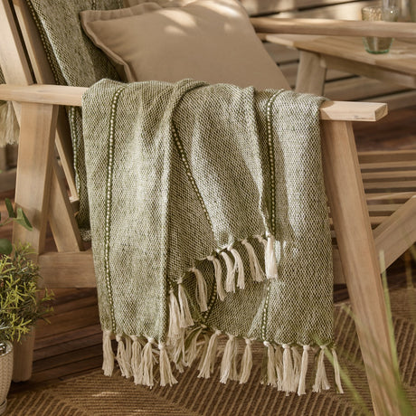 Hedon Striped Polyester Throw in moss green with knotted fringe, draped over a wooden chair on an outdoor patio setting.