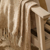 Hedon Striped Polyester Throw in Natural draped over a wooden chair arm, showing woven texture with subtle stripes and knotted fringe detail.