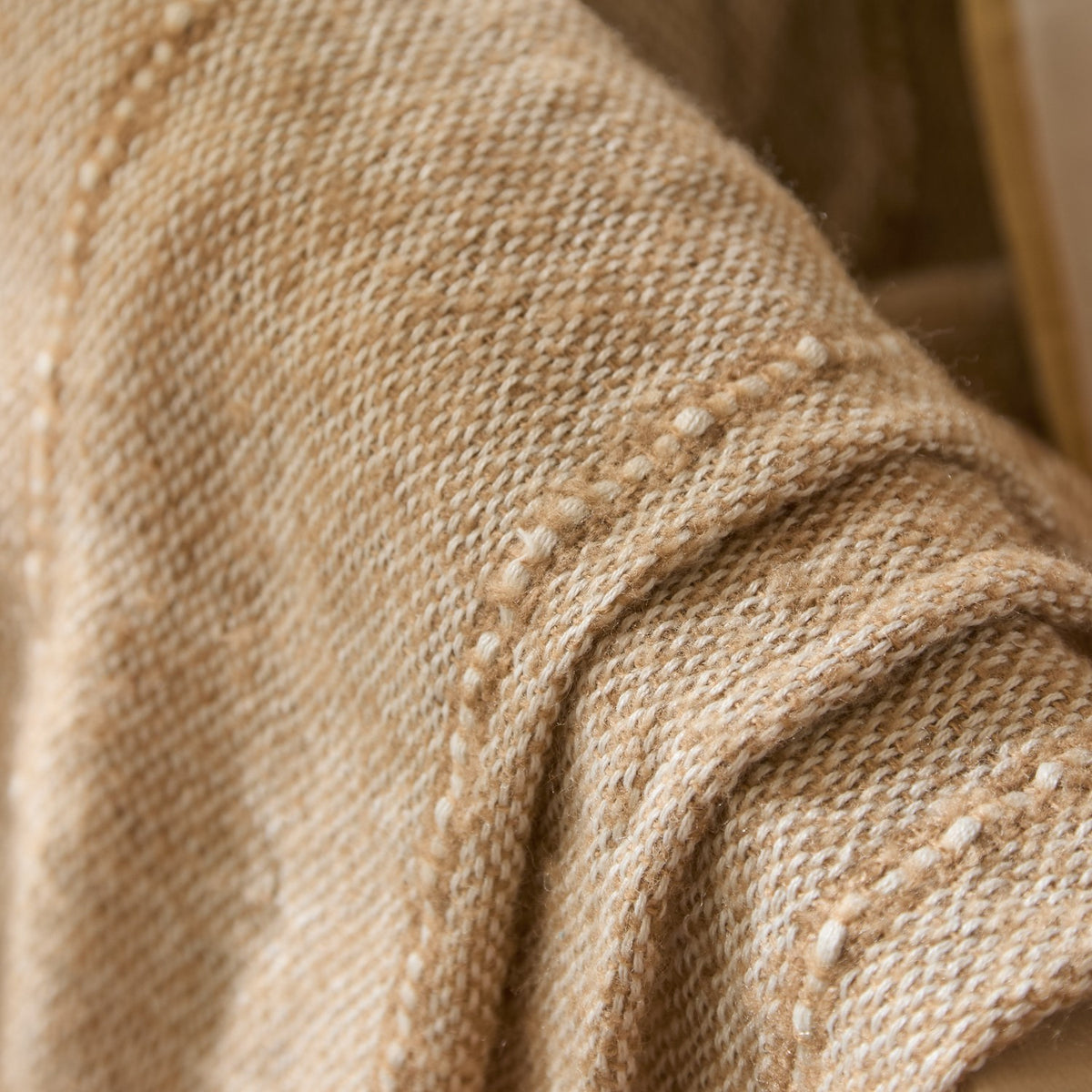 Close-up of the Hedon Striped Polyester Throw in Natural, showing its woven sand-tone texture with pale cream flecks and a subtle linear stripe detail.