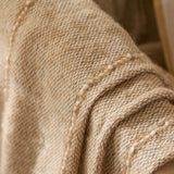 Close-up of the Hedon Striped Polyester Throw in Natural, showing its woven sand-tone texture with pale cream flecks and a subtle linear stripe detail.