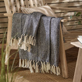 Hedon Striped Polyester Throw in navy and cream marl with knotted fringe, draped over a wooden armchair beside a striped cushion in an outdoor living space.
