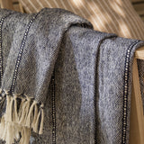 Hedon Striped Polyester Throw in navy and cream marl with knotted fringe, draped over a wooden chair outdoors.