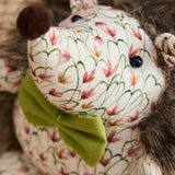 Henrietta hedgehog polyester door stop, close-up of face with cream floral fabric, black bead eyes, brown pom-pom nose, olive-green bow, and shaggy faux fur trim.