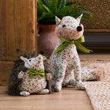 Henrietta hedgehog-shaped polyester door stop with faux fur back, cream floral fabric, olive-green bow, shown beside a matching floral fox decor piece in a hallway setting.