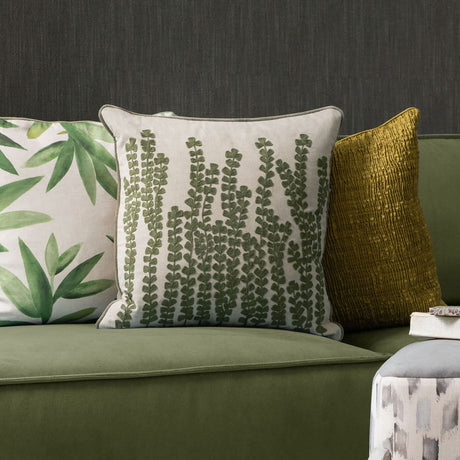 Herb Velvet Linen Cushion in Sage, a square cushion with embroidered fern-like fronds in green thread on a natural linen-cotton ground, shown on a green sofa beside patterned and mustard cushions.