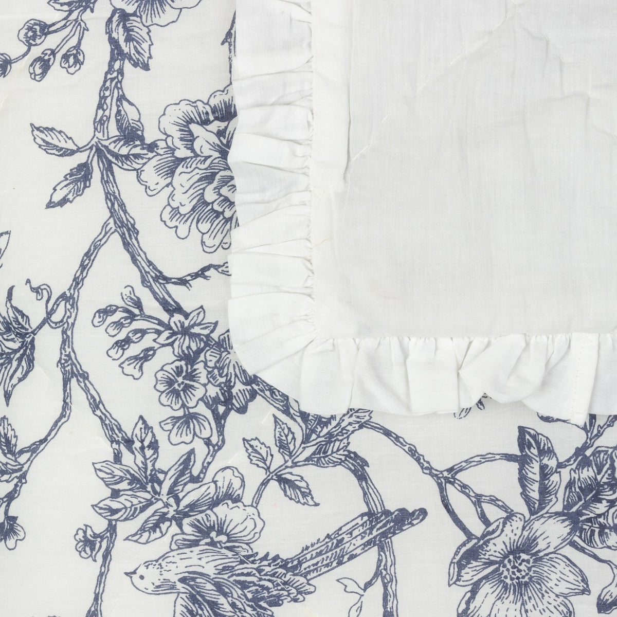 Hermione linen cotton bedspread corner in ivory blue, showing Toile de Jouy floral and bird print beside a plain quilted panel with a frilled ruffle edge.