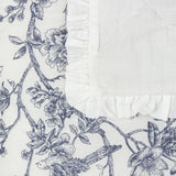Hermione linen cotton bedspread corner in ivory blue, showing Toile de Jouy floral and bird print beside a plain quilted panel with a frilled ruffle edge.