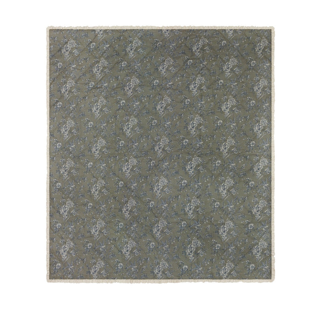 Hermione Linen Cotton Bedspread in Moss, a quilted throw-over with cream and blue Toile de Jouy floral print, finished with a cream ruffled frill edge on a plain background.