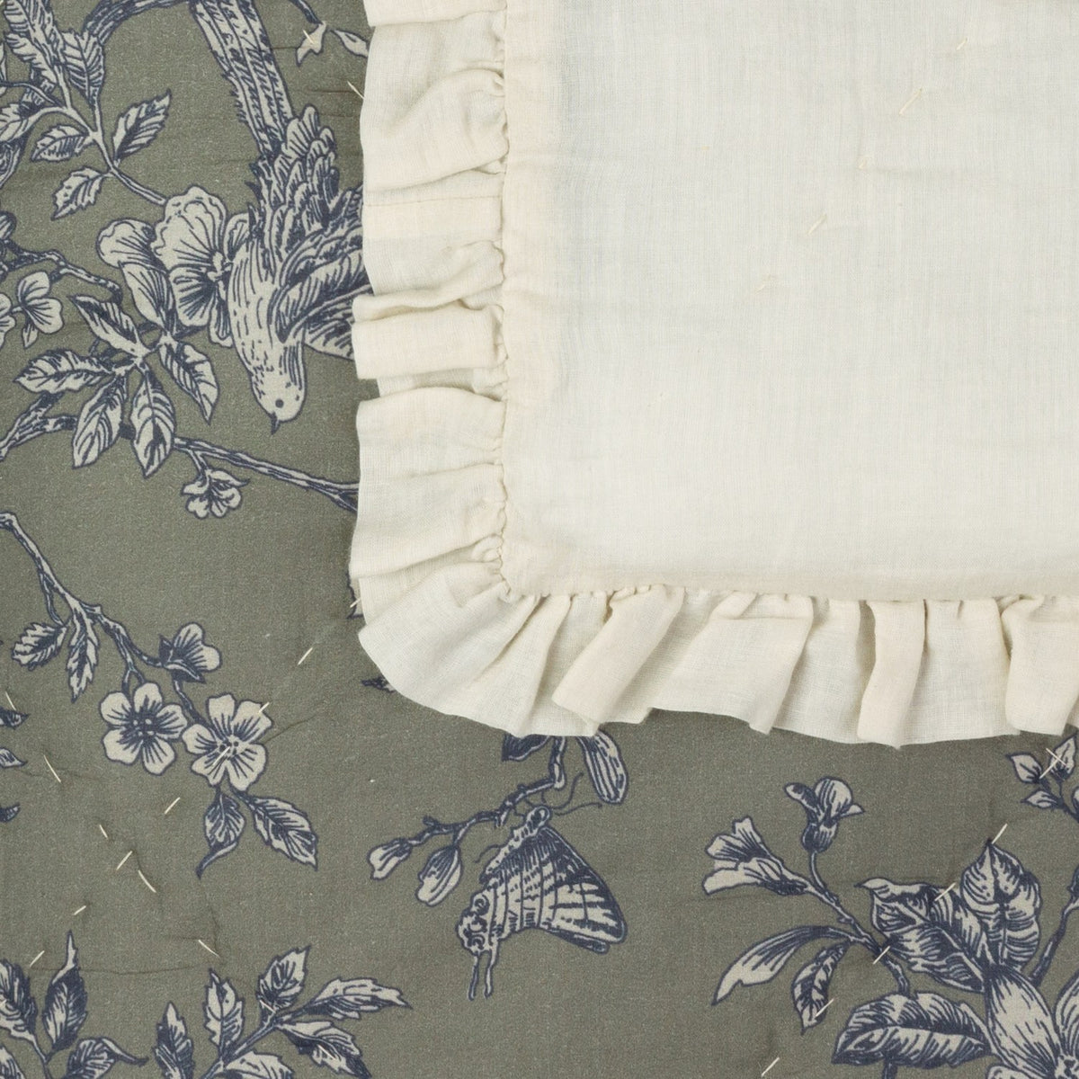 Hermione Linen Cotton Bedspread in Moss, corner detail showing cream ruffled frill edging and moss-green cotton with blue and cream Toile de Jouy floral, bird and butterfly print.