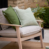 Hessle Stripe Yarn-Dyed Cotton Cushion in eucalyptus green and white, styled on a wooden outdoor armchair beside a plain olive green cushion.