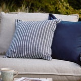 Hessle Stripe Yarn-Dyed Cotton Cushion in navy with white pinstripes and oxford edge, shown on a light grey outdoor sofa beside a plain navy cushion.