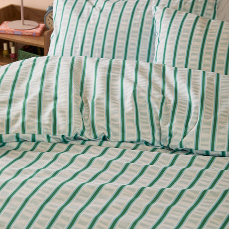 Hettie Printed Striped Duvet Cover Set in green and white on a bed with matching pillowcases, showing a vertical seersucker-effect stripe print in a bedroom setting.